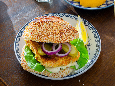 Sesam-Brötchen belegt mit Backvisch und Salat auf einem Teller mit Dekoration.