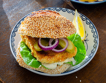Sesam-Brötchen belegt mit Backvisch und Salat auf einem Teller mit Dekoration.