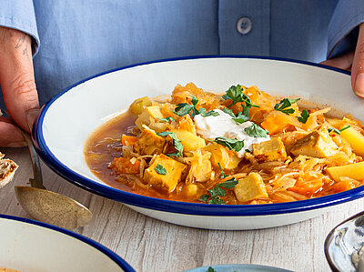 2 Suppenteller mit Kartoffeln, Sojawürfeln und Sauerkraut mit Tischdekoration. An einem Teller 2 Hände.