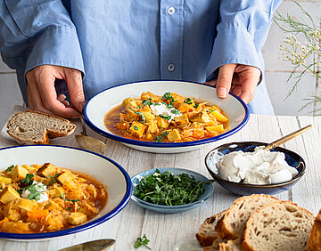 2 Suppenteller mit Kartoffeln, Sojawürfeln und Sauerkraut mit Tischdekoration. An einem Teller 2 Hände.