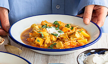 2 Suppenteller mit Kartoffeln, Sojawürfeln und Sauerkraut mit Tischdekoration. An einem Teller 2 Hände.