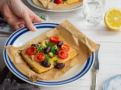 Tofuscheiben belegt mit Tomaten und Oliven und Kräutern auf einem Teller mit Dekoration.