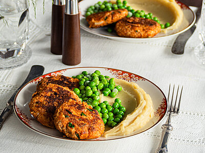 Tofu-Frikadellen mit Kartoffelpüree und Erbsen auf 2 Tellern mit Tischdekoration.