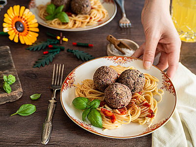 Tofu-Bällchen auf Spaghetti mit Tomatensoße mit Tischdekoration auf 2 Tellern.