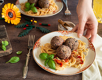 Tofu-Bällchen auf Spaghetti mit Tomatensoße mit Tischdekoration auf 2 Tellern.