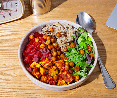 Tofuwürfel mit rote Bete Würfel, Kichererbsen und Salat an Reis in einer Schüssel mit Tischdekoration.