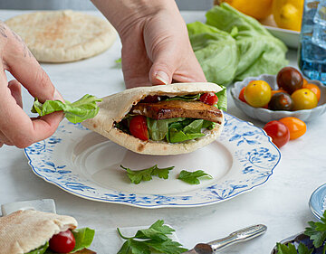 Pitataschen mit Tofu und Salat auf 1 Teller und 1 Holzbrett mit Tischdekoration.