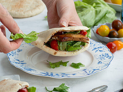 Pitataschen mit Tofu und Salat auf 1 Teller und 1 Holzbrett mit Tischdekoration.