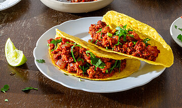 3 Tacos mit rotem Sojagehacktem auf Tellern mit Tischdekoration.