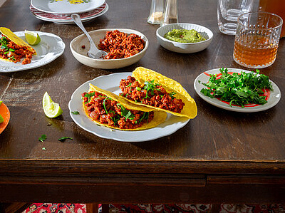 3 Tacos mit rotem Sojagehacktem auf Tellern mit Tischdekoration.