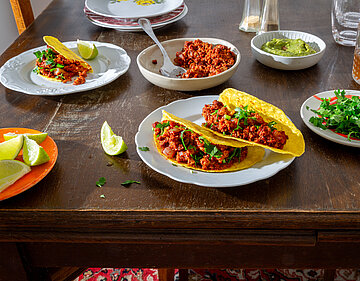 3 Tacos mit rotem Sojagehacktem auf Tellern mit Tischdekoration.