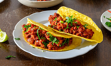 3 Tacos mit rotem Sojagehacktem auf Tellern mit Tischdekoration.