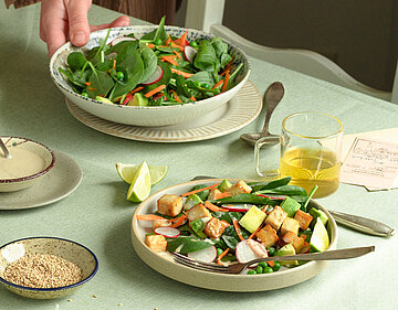 Crispy Tofu-Salat mit Tahini-Dressing Tofu-Würfel mit Salat auf Tellern mit Dip und Tischdekoration.