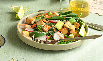 Tofu-Würfel mit Salat auf Tellern mit Dip und Tischdekoration.