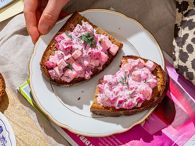 Roter Tofu-Heringssalat auf Brotscheiben auf einem Teller mit Tischdekoration.