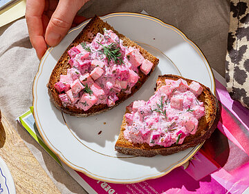 Roter Tofu-Heringssalat auf Brotscheiben auf einem Teller mit Tischdekoration.
