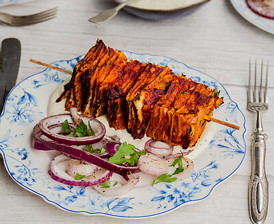 Tofu-Spieß mit Zwiebeln und Kräutern auf einem Teller mit Dip und Tischdekoration.