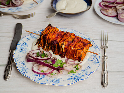 Tofu-Spieß mit Zwiebeln und Kräutern auf einem Teller mit Dip und Tischdekoration.