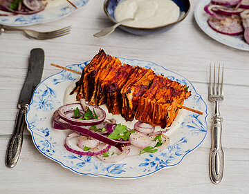 Tofu-Spieß mit Zwiebeln und Kräutern auf einem Teller mit Dip und Tischdekoration.