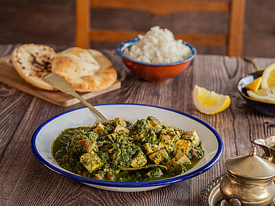 Tofuwürfel mit Spinat-Soße auf einem Teller mit kleinen Schüsseln auf einem Holztisch.