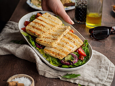3 gegrillte Tofuscheiben auf Salat in einer Schüssel mit Tischdekoration.