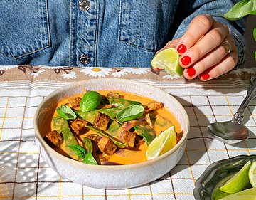 Eine Schüssel mit einem Curry auf einem Tischtuch mit Deko.