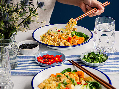Nudeln mit Tofuwürfel und Fenchel an buntem Gemüse auf 2 Tellern, die auf einem Tisch stehen, mit Dekoration.