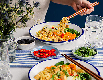 Nudeln mit Tofuwürfel und Fenchel an buntem Gemüse auf 2 Tellern, die auf einem Tisch stehen, mit Dekoration.