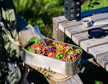 Tofuwürfel, rote Linsen, Salat und Rote Bete in einer Metallschüssel auf der Lehne eines Holzstuhls im Garten.
