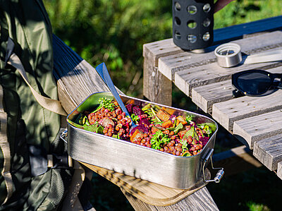 Tofuwürfel, rote Linsen, Salat und Rote Bete in einer Metallschüssel auf der Lehne eines Holzstuhls im Garten.