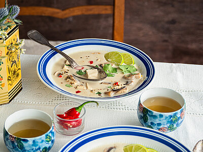 Helle Suppe in einem Teller mit Tofu-Stückchen, Zotrone und Pilzen mit Tischdekoration.