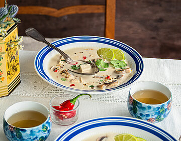 Helle Suppe in einem Teller mit Tofu-Stückchen, Zotrone und Pilzen mit Tischdekoration.