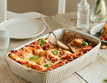 Lasagne in einer Auflaufform und auf Tellern mit Dekoration.