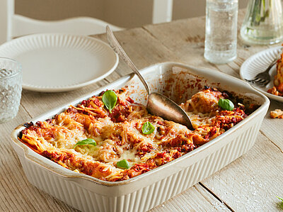 Lasagne in einer Auflaufform und auf Tellern mit Dekoration.