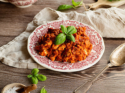 Tofu mit dicker roter Sauce mit Basilikum auf einem Teller und Dekoration.