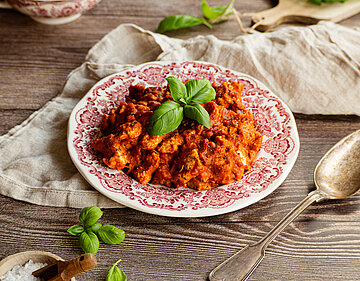 Tofu mit dicker roter Sauce mit Basilikum auf einem Teller und Dekoration.