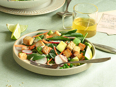 Tofu-Würfel mit Salat auf Tellern mit Dip und Tischdekoration.