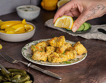 Gelbe Tofuwürfel auf einem Teller mit Zitrone und Gurke und Dekoration.