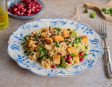 Couscous mit Tofustückchen Lauch, Petersiele und Grantapfelkernen auf 2 Tellern mit Tischdekoration.