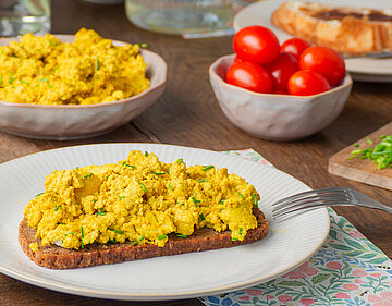 Eine Brotscheibe mit zerbröseltem, gewürztem Tofu und Kräutern. 