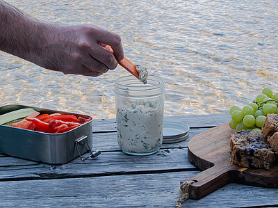 Weißes Kräuterdipp mit Gemüsestreifen auf einem Holztisch und Dekoration.