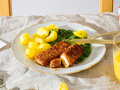 Tofustäbchen mit Panade auf einem Teller mit Kartoffeln und Spinat mit Tischdekoration.
