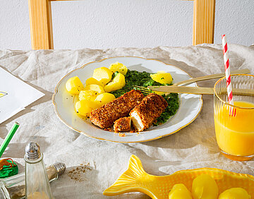 Vischstäbchen Tofustäbchen mit Panade auf einem Teller mit Kartoffeln und Spinat mit Tischdekoration.