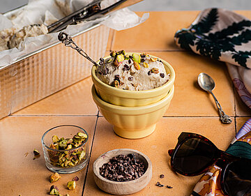 Hellbraune Creme in einer Schale mit Nuss-Topping in einem Schälchen und Tischdekoration.