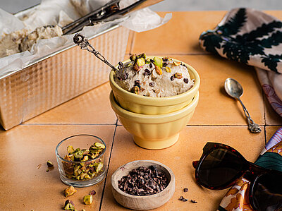 Hellbraune Creme in einer Schale mit Nuss-Topping in einem Schälchen und Tischdekoration.