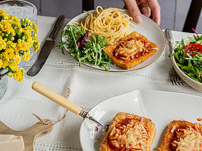 Teller mit Nudeln und einer Tofuscheibe, darauf Tomatensoße und Käse an Salat.