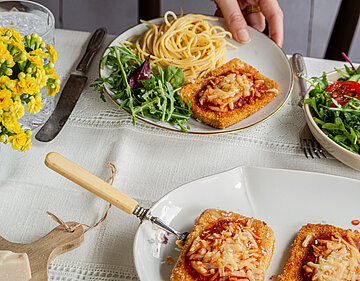 Parmigiana Teller mit Nudeln und einer Tofuscheibe, darauf Tomatensoße und Käse an Salat.