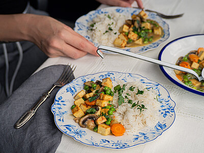 Tofustückchen, Pilze, Möhren und Erbsen an Reis auf einem Teller mit Tischdekoration.