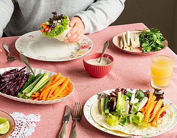 Teller mit Wraps und Gemüse auf einem Tischtuch.
