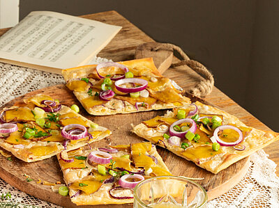 Vlammkuchen auf 2 Tellern und einem Holzbrett mit Zweibeln, Tofu und Lauch mit Tischdekoration.